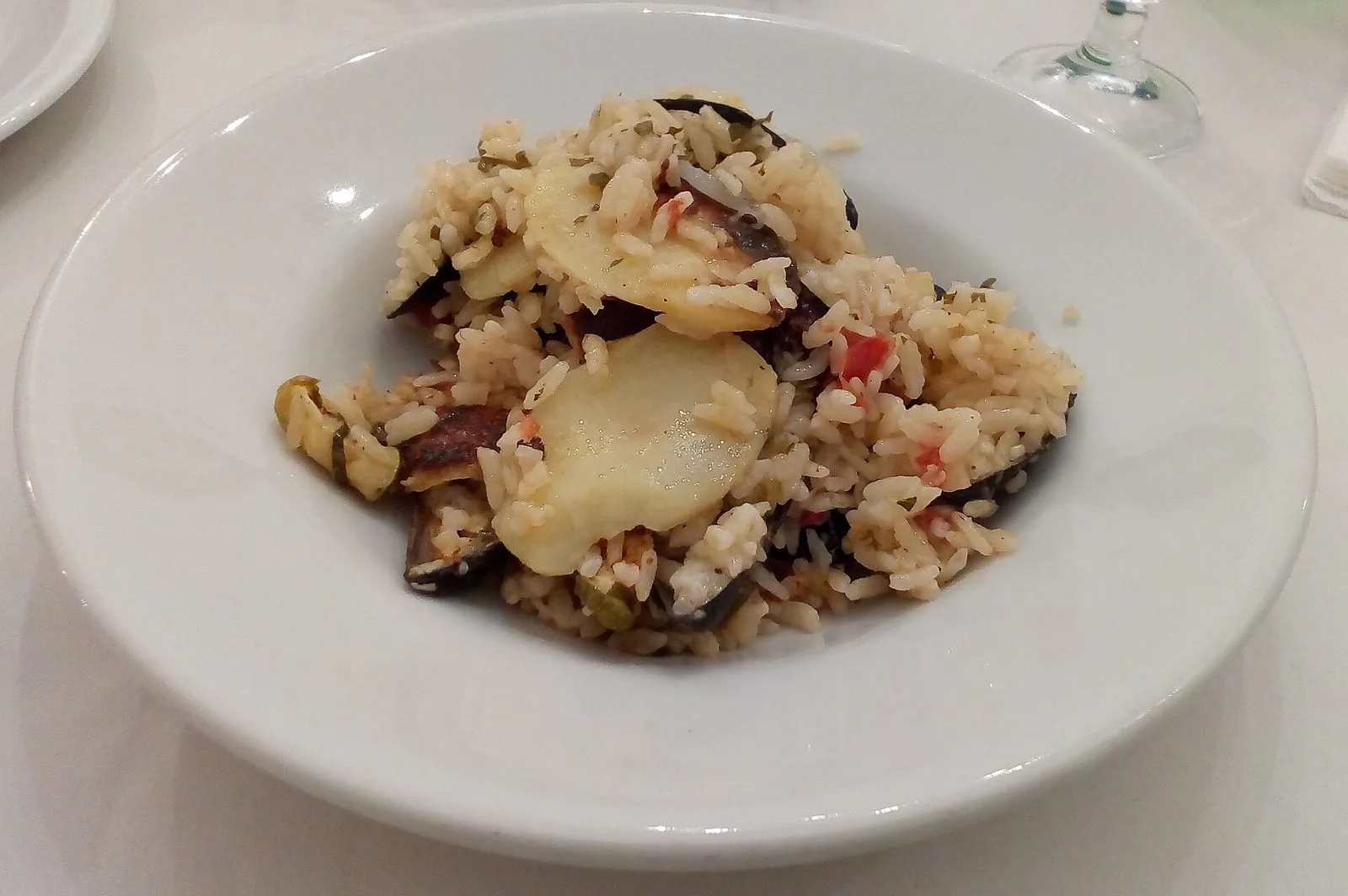 Un piatto bianco con riso, fette di patate e cozze con il guscio, condito con pomodoro e prezzemolo