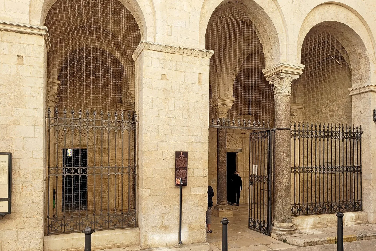 Il portico ad archi della Chiesa di Ognissanti a Trani, in pietra chiara, con cancellate in ferro battuto e una colonna con capitello scolpito