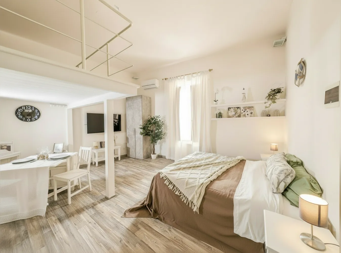 Il monolocale con il letto matrimoniale, il tavolo bianco, la TV a parete e il soppalco con la ringhiera